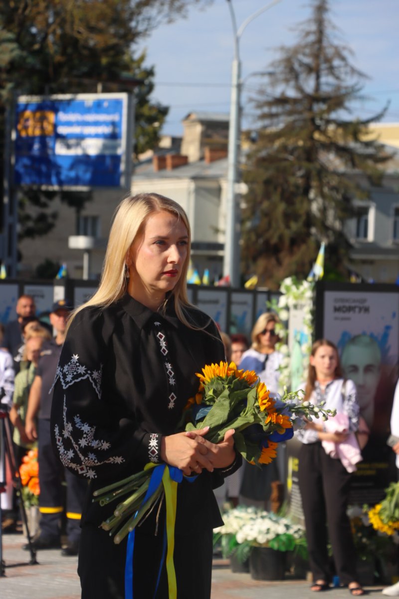 Жінка у вишитій сорочці тримає соняхи  руках.